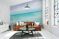Turquoise Ocean wallpaper mural behind a tan leather sofa and round glass coffee table in a bright living room