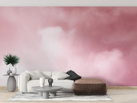 Pink Sky And Clouds wallpaper in blush tones behind a white sofa and brown leather pouf in a living room
