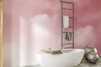 Pink Sky And Clouds wallpaper in soft pink cloud tones behind a white freestanding bathtub and towel ladder in a bathroom