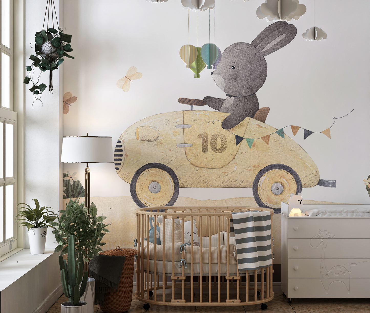 Playful Bunny Car Ride Kids wallpaper mural above a wood oval crib and white dresser in a bright nursery