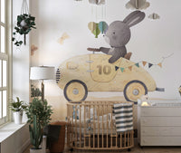Playful Bunny Car Ride Kids wallpaper mural above a wood oval crib and white dresser in a bright nursery