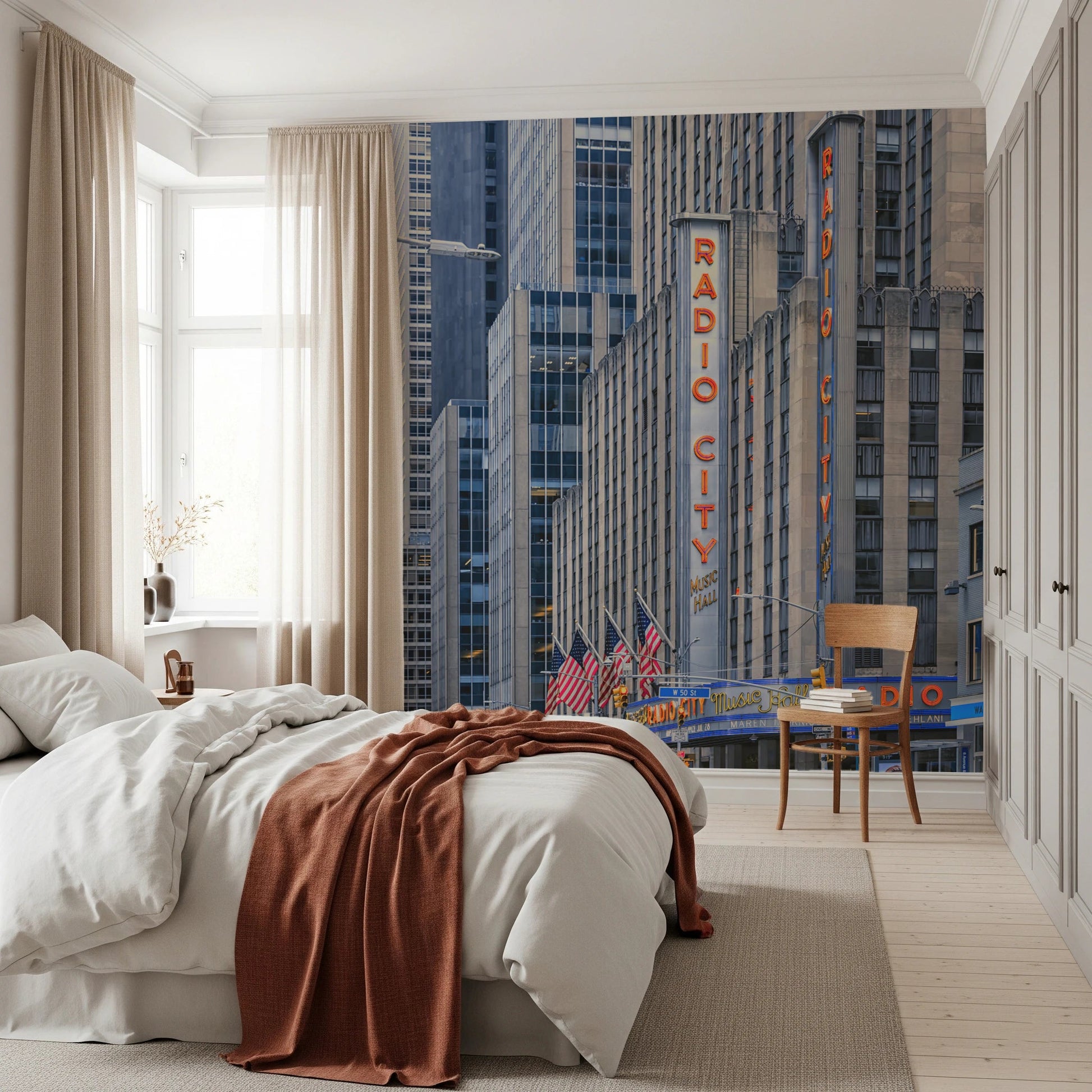 Radio City's Glow wallpaper mural of the Radio City sign and NYC towers behind a white bed with rust throw in a bedroom