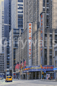 Radio City's Glow wallpaper mural shown full-wall with the red Radio City Music Hall sign, flags and a yellow taxi below