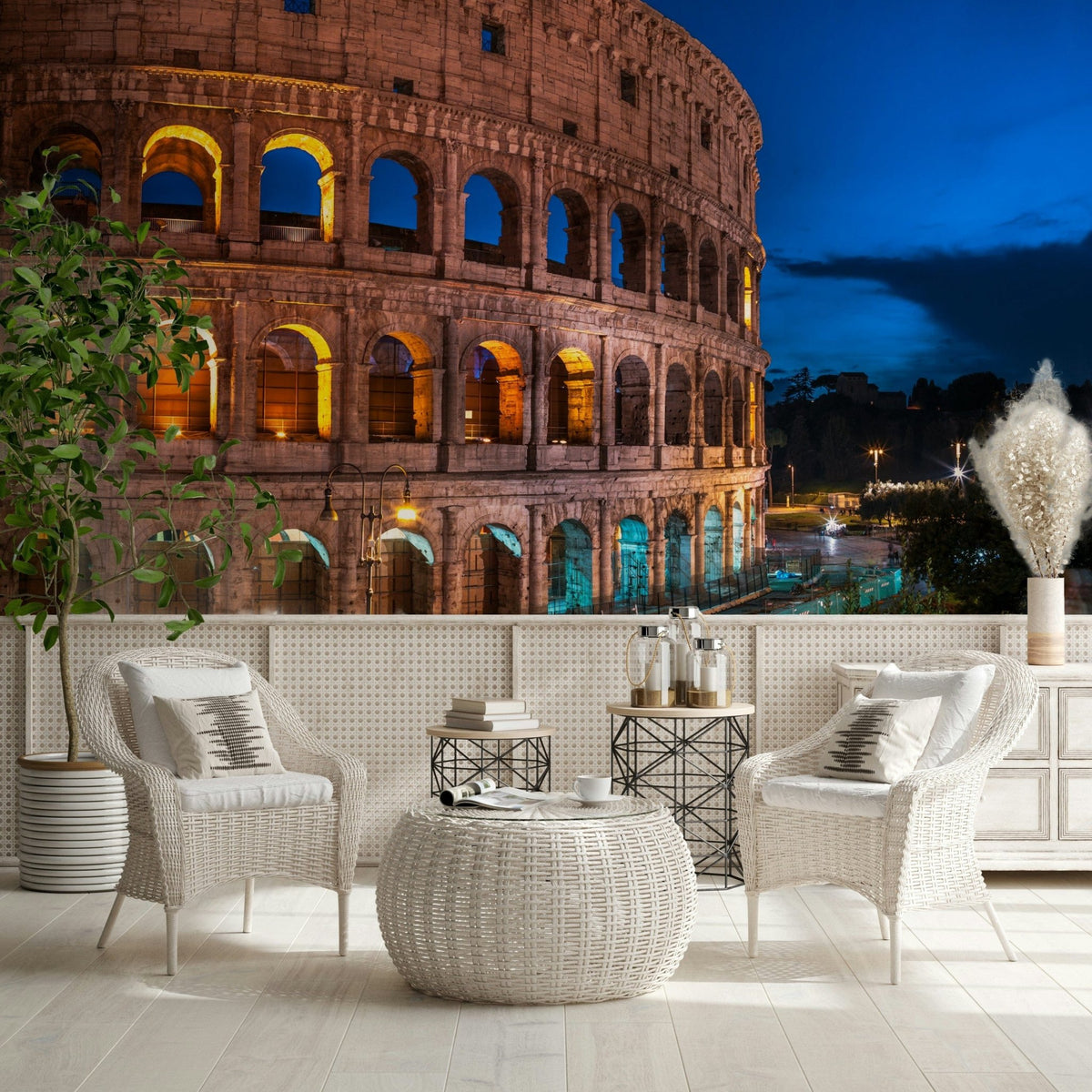 Roman Nights wallpaper mural of the lit Colosseum at night behind white wicker chairs on a patio terrace