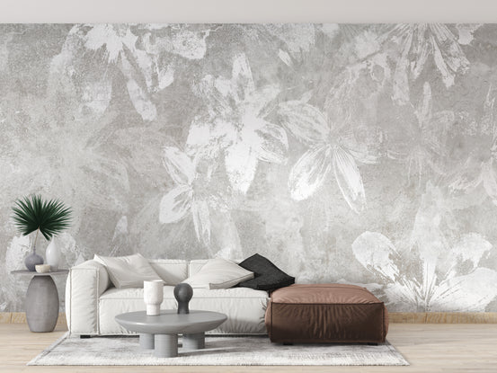 Rustic White Flower wallpaper mural with grey concrete texture behind a white sofa and brown leather pouf in a living room