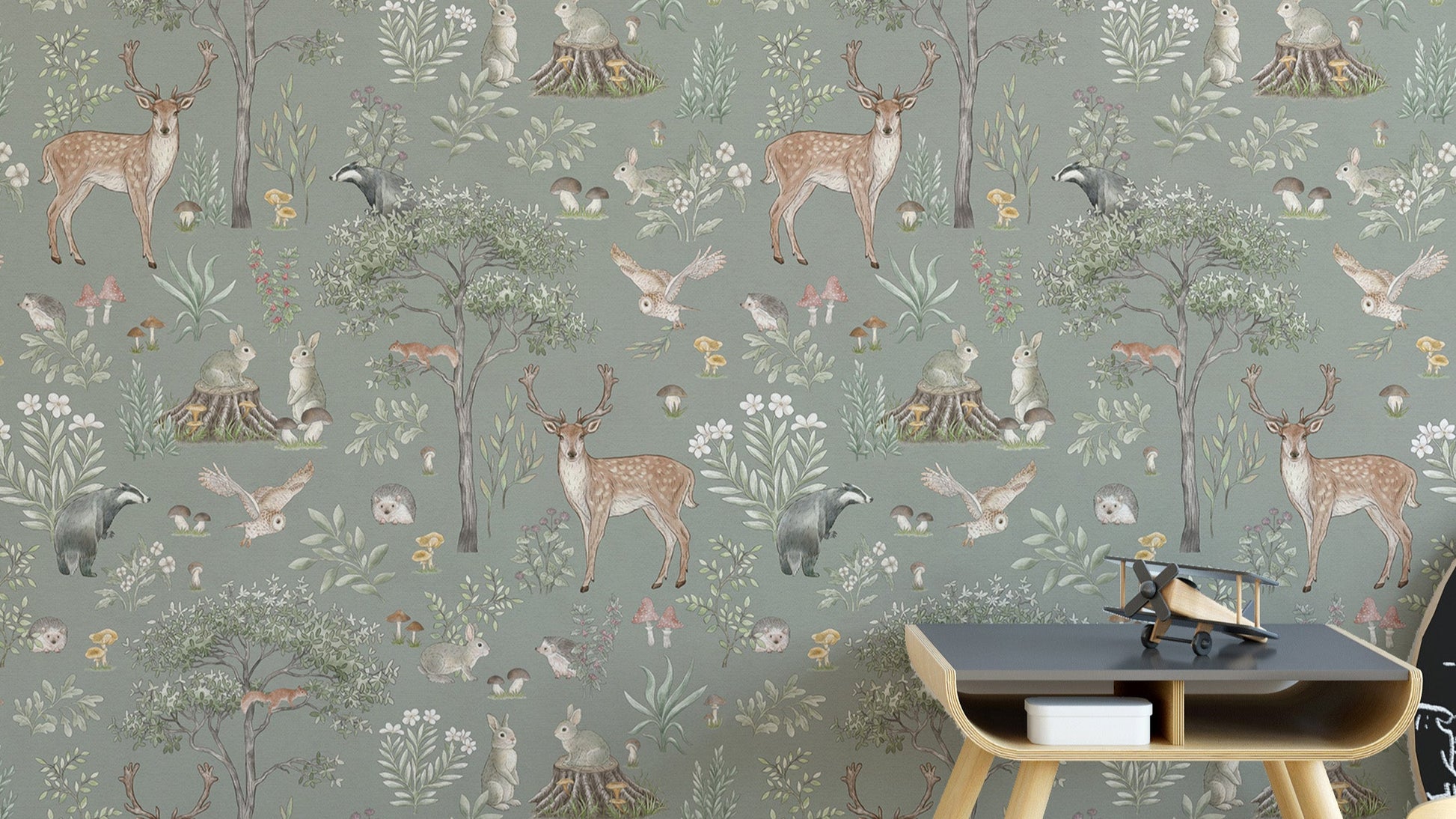 Sage Green Wildlife wallpaper with deer, badgers and owls behind a dark wood side table in a kids room