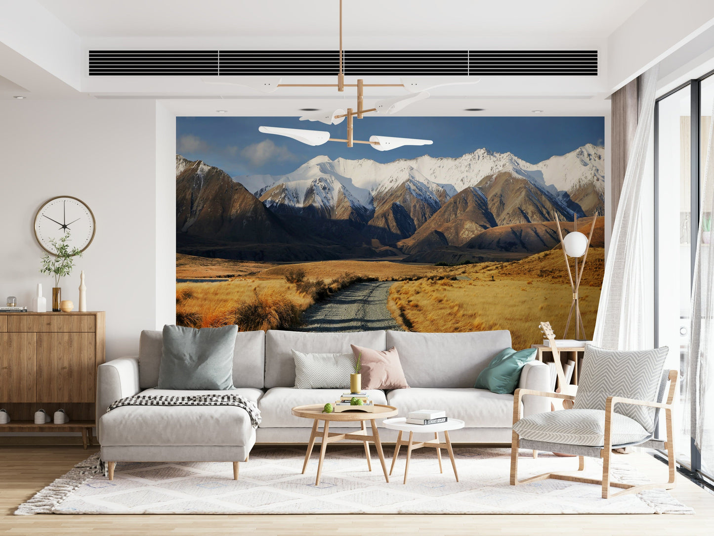 Snowy Peaks Path wallpaper mural of snowy mountains and a valley path behind a gray sectional and woven armchair