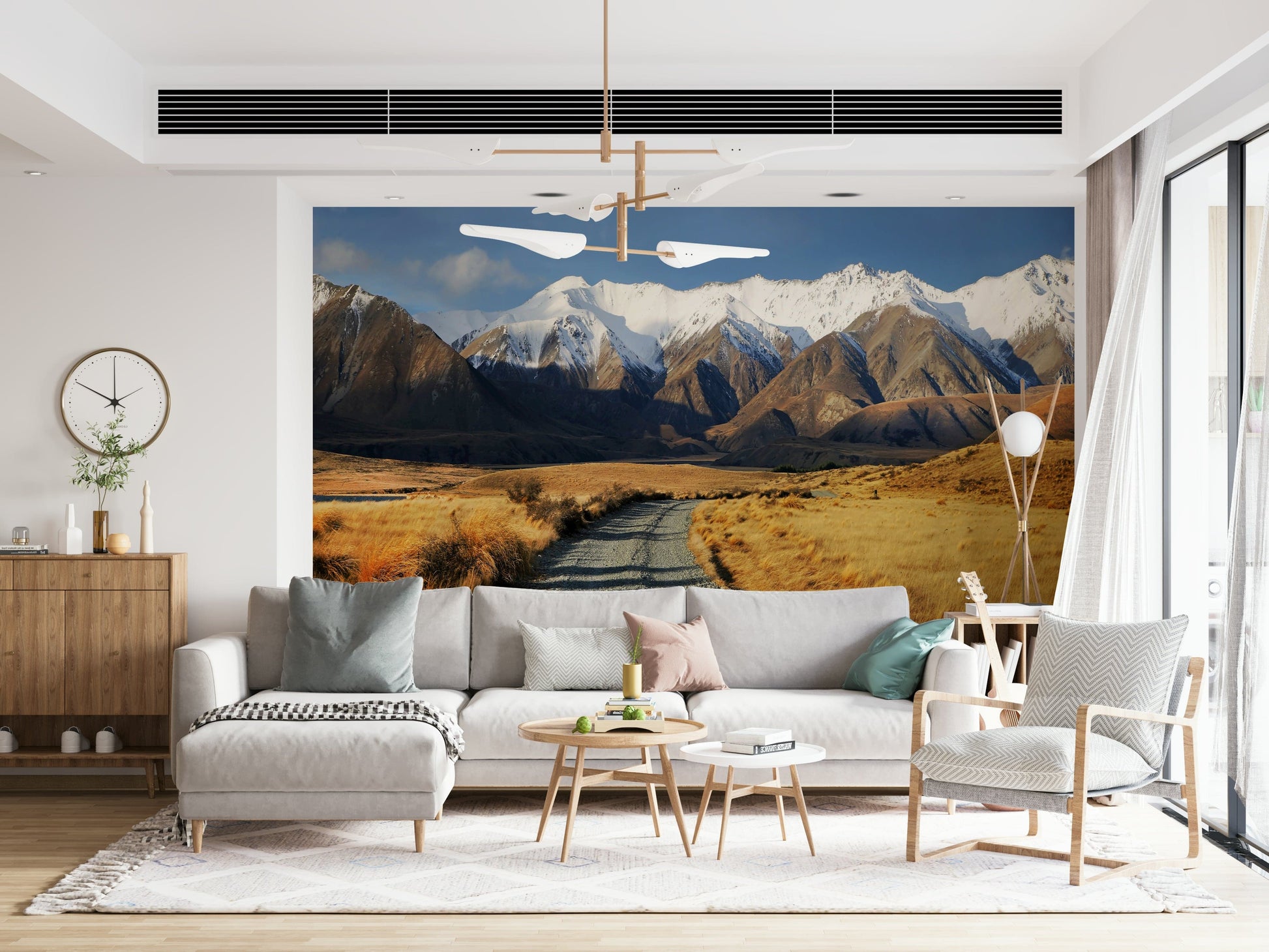 Snowy Peaks Path wallpaper mural of snowy mountains and a valley path behind a gray sectional and woven armchair