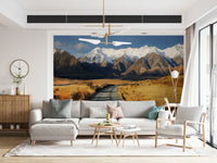 Snowy Peaks Path wallpaper mural of snowy mountains and a valley path behind a gray sectional and woven armchair