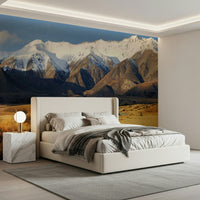 Snowy Peaks Path wallpaper mural of snowy mountains and golden valley behind a cream upholstered bed in a bedroom