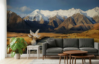 Snowy Peaks Path wallpaper mural of snowy mountains and golden valley behind a gray sofa in a bright living room