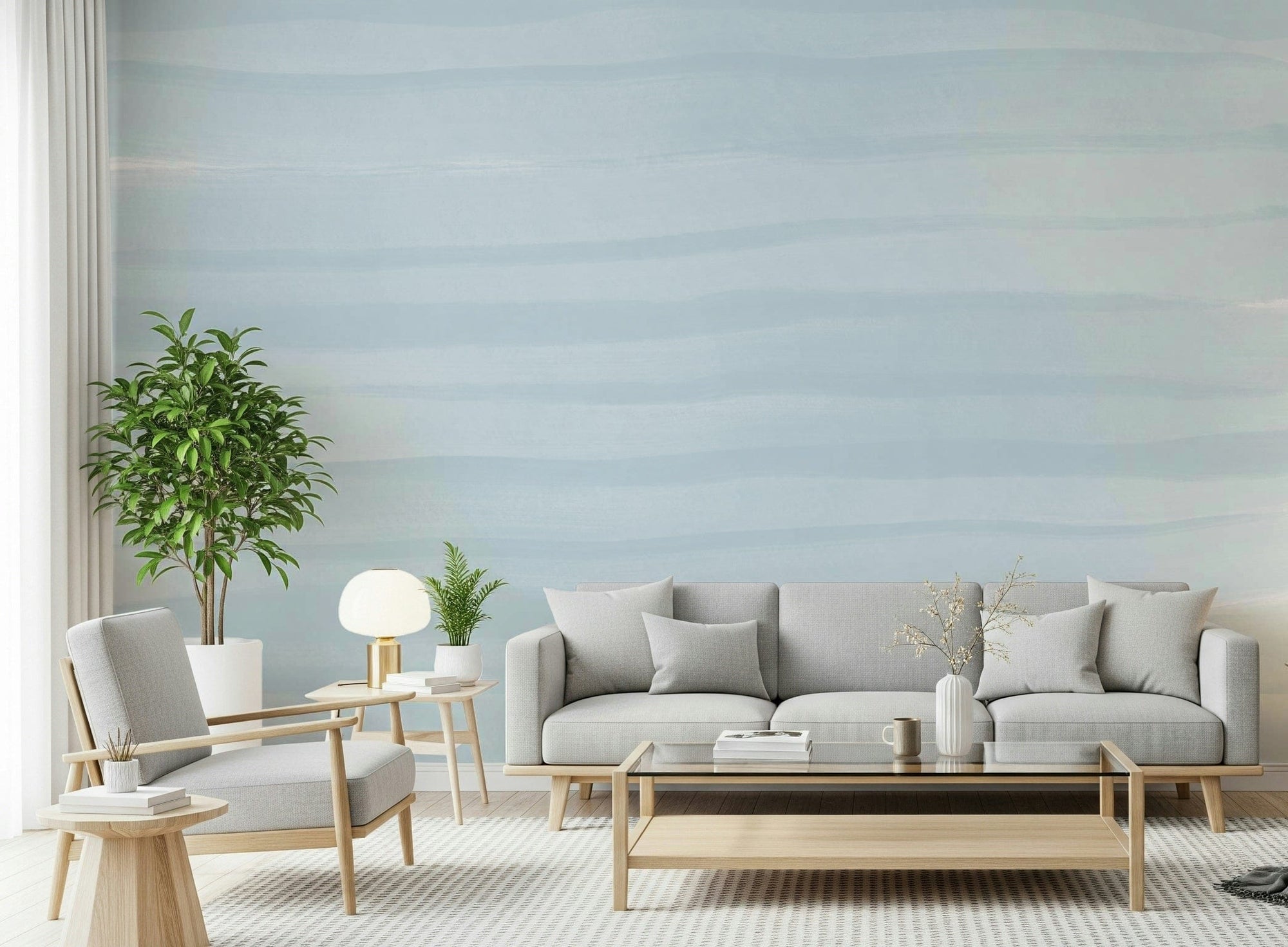 Soft Blue Tide wallpaper mural of pale watercolor sea bands behind a grey sofa and wood armchair in a living room