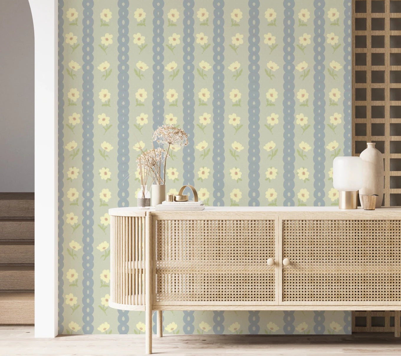 Soft Daisy Stripes wallpaper in green and blue daisy stripes behind a rattan cane sideboard with dried flowers in an entryway