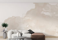 Abstract Watercolor wallpaper mural in soft beige washes behind a white sofa and brown leather pouf in a living room