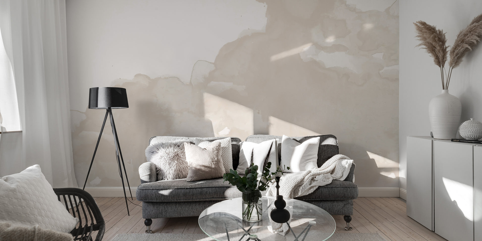 Abstract Watercolor wallpaper mural in cream tones behind a gray sofa and black tripod lamp in a living room