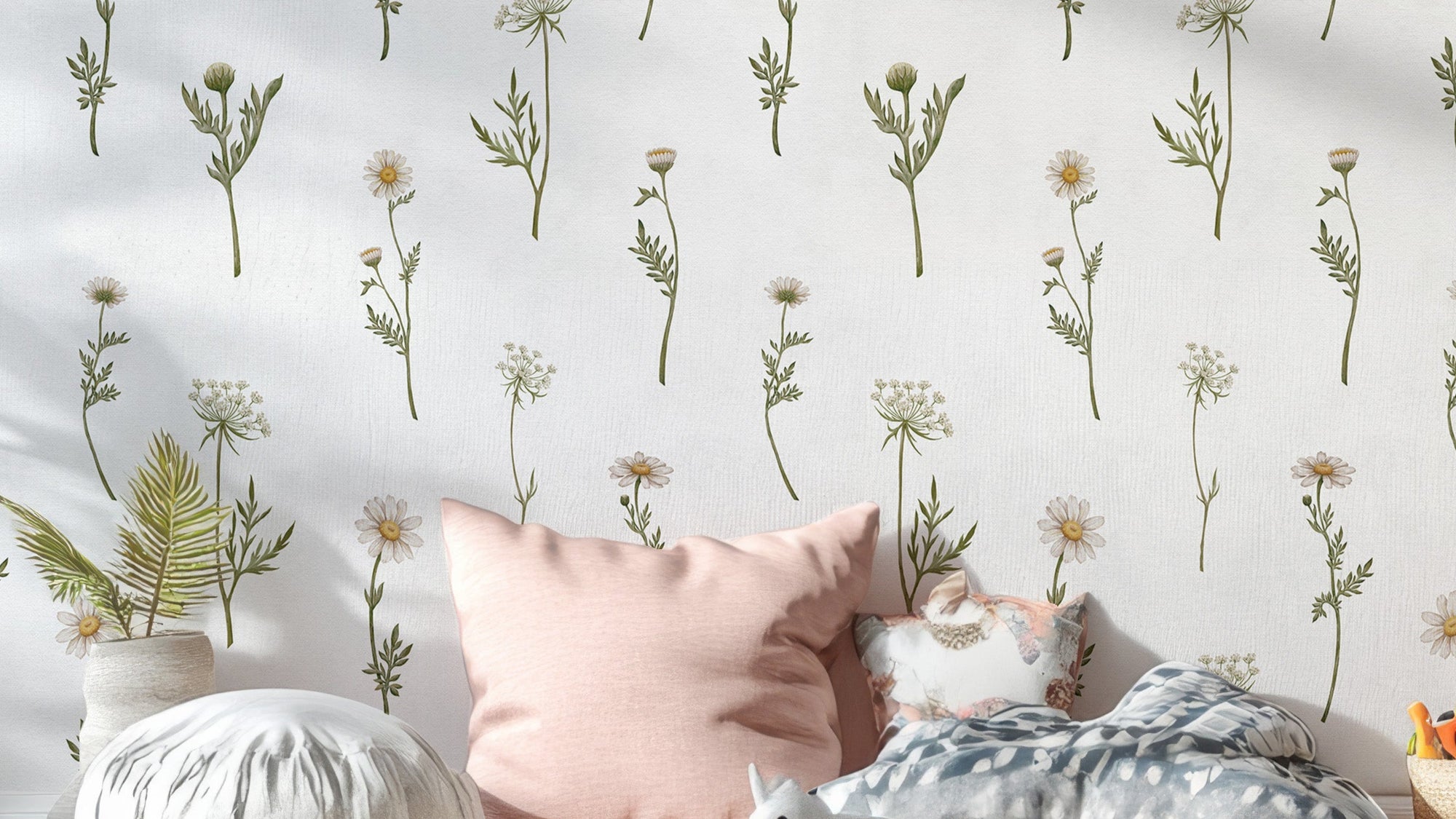 Soft White Wildflower wallpaper close-up behind a bed with a pink cushion showing green daisy stems