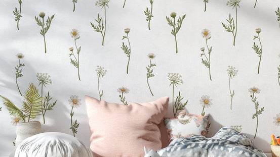 Soft White Wildflower wallpaper close-up behind a bed with a pink cushion showing green daisy stems
