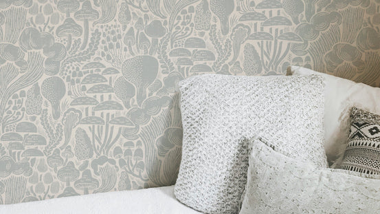 Sten Fungi Forest Silhouettes wallpaper in sage green behind a white bed with textured lace cushions