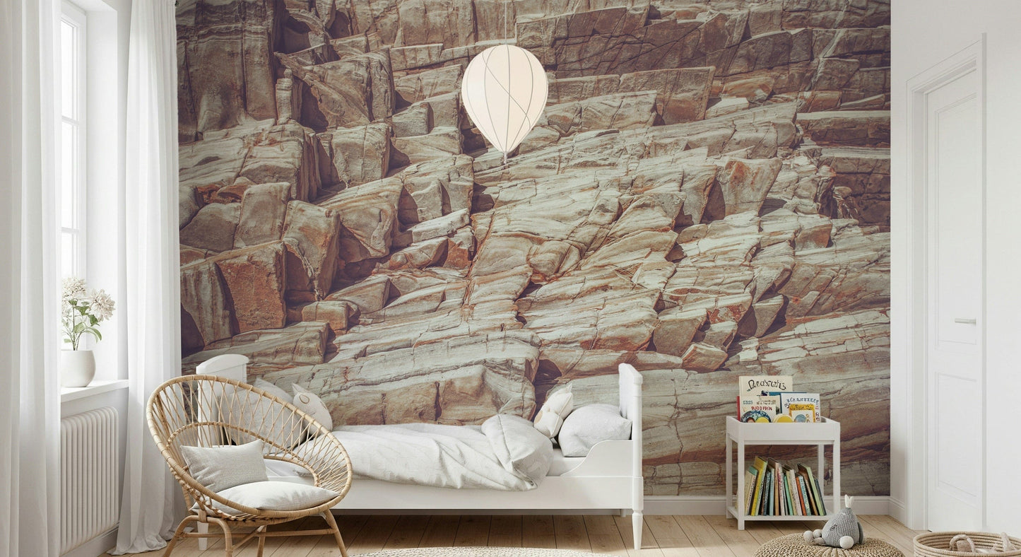 Striated Rock Face wallpaper mural of sandy rock layers behind a white bed and rattan chair in a child's room