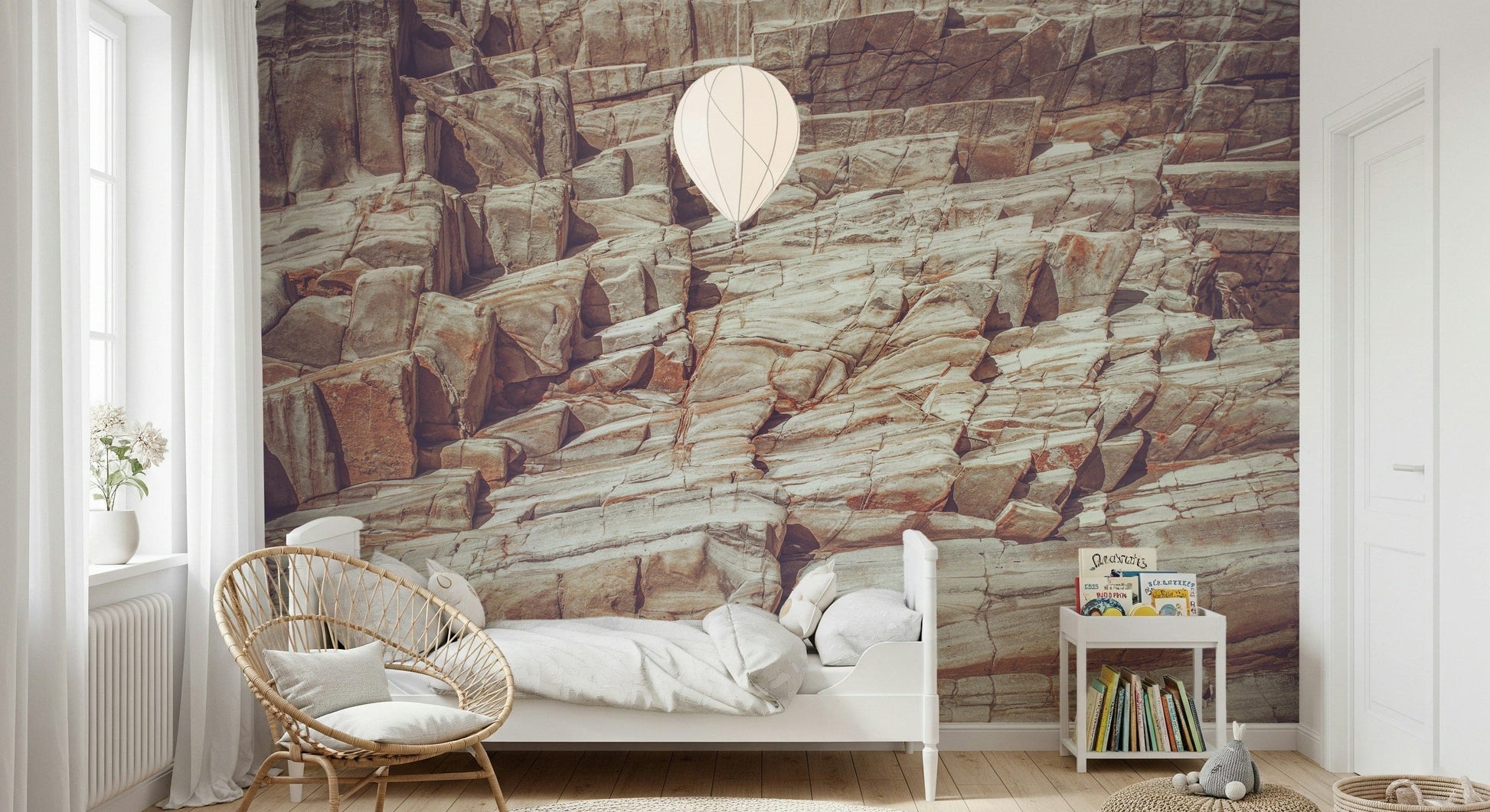 Striated Rock Face wallpaper mural of sandy rock layers behind a white bed and rattan chair in a child's room
