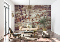 Striated Rock Face wallpaper mural of red and cream rock behind a cane bench sofa and olive tree on tile floor