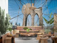 Strolling Across the Brooklyn Bridge wallpaper mural in a cafe lounge with live-edge wood tables, stools and a cactus