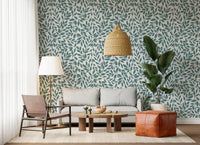 Teal Vines wallpaper with teal foliage behind a grey sofa, leather sling chair and fan palm in a living room