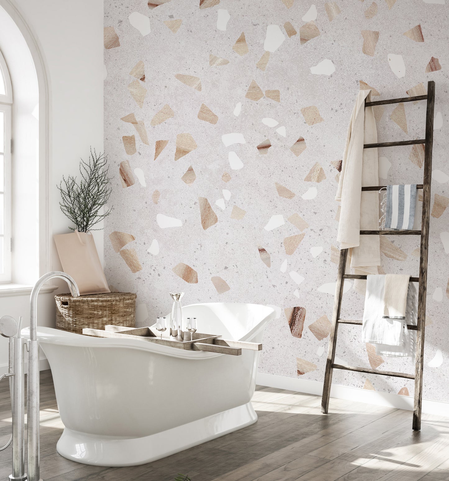 Terrazzo Marble Tile wallpaper mural in neutral tones behind a white roll-top bathtub and rustic towel ladder