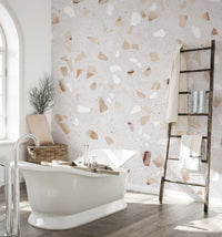 Terrazzo Marble Tile wallpaper mural in neutral tones behind a white roll-top bathtub and rustic towel ladder