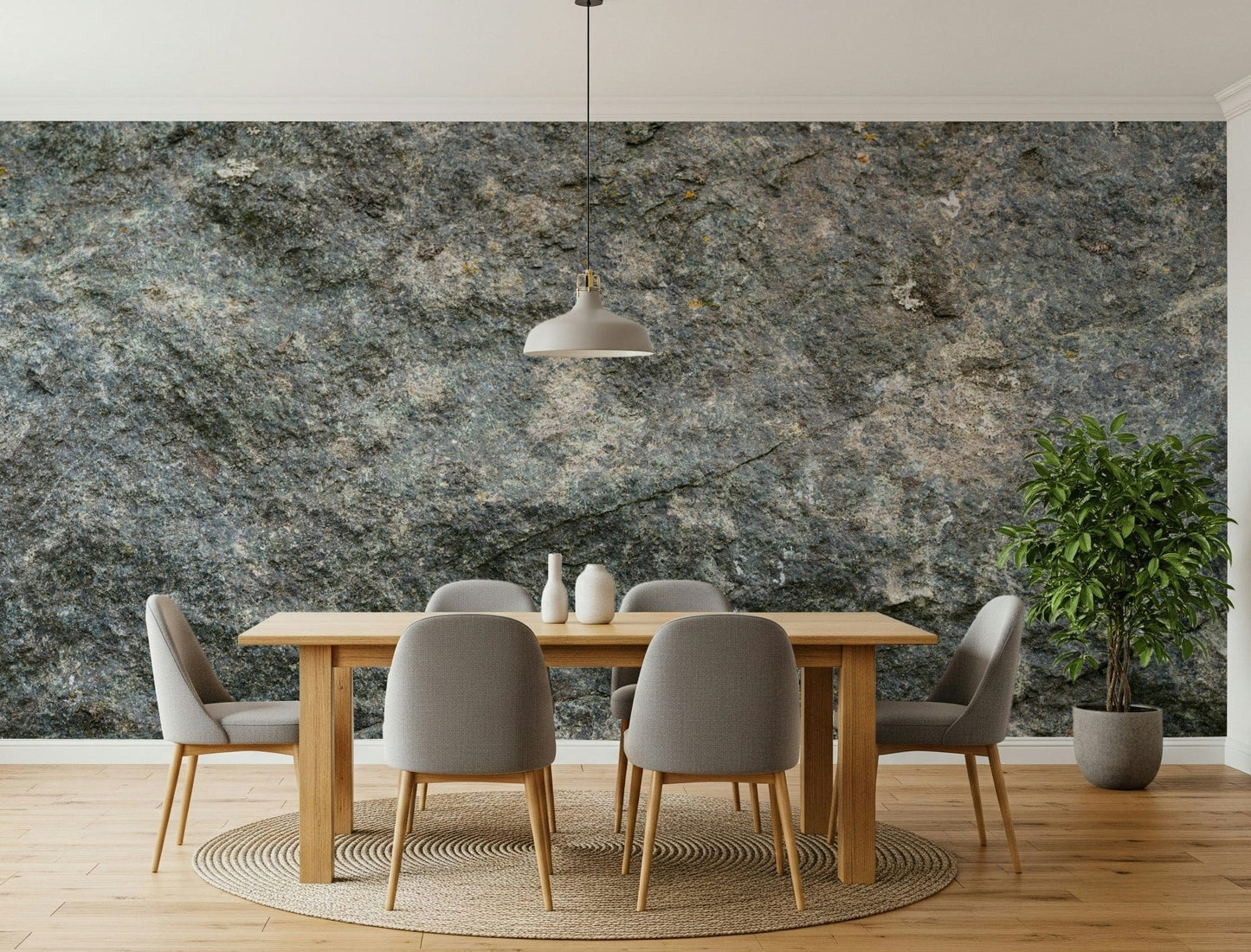 Textured Rock wallpaper mural in grey-green stone behind a wood dining table with grey chairs and a ficus tree