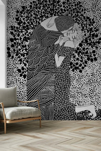 The Kiss II wallpaper mural of an embracing couple in black and white behind a beige wood-frame armchair