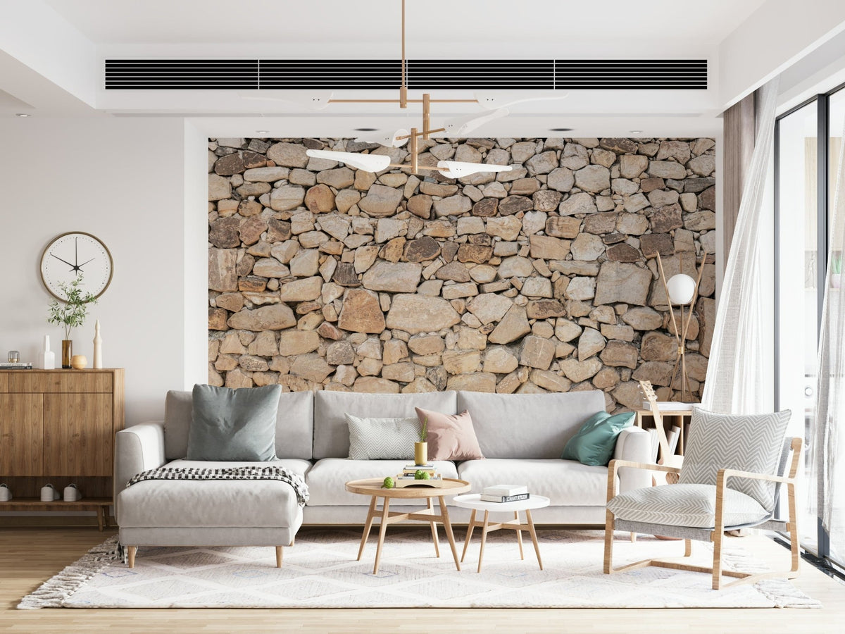 Timeless Stonework wallpaper mural in tan fieldstone behind a grey sofa with sage and pink pillows in a living room
