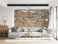 Timeless Stonework wallpaper mural in tan fieldstone behind a grey sofa with sage and pink pillows in a living room