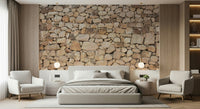 Timeless Stonework wallpaper mural in tan fieldstone behind a grey bed flanked by two white armchairs in a bedroom