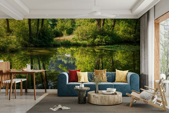 Tranquil Nature Reflection wall mural of trees mirrored in a pond behind a navy sofa with red and yellow pillows