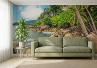 Tropical Shores wallpaper mural of green palms and rocky shore behind a sage green leather sofa in a living room