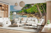 Tropical Shores wallpaper mural with palms and sea behind a long white sofa and rattan pendant lights in a living room