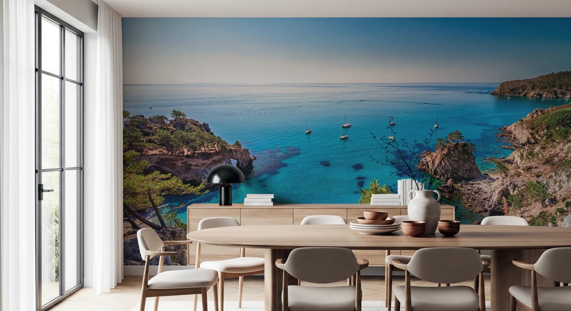 Turquoise Cove Escape wallpaper mural with sailboats and cliffs behind a wood dining table and sideboard