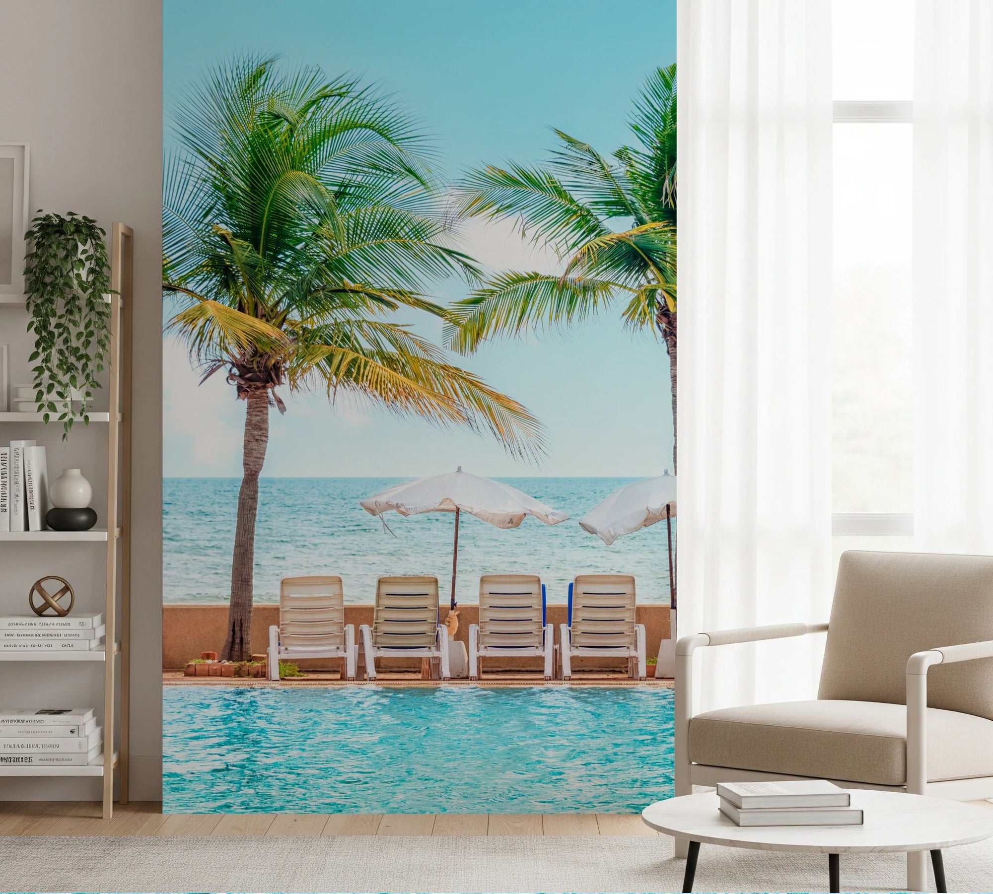 Turquoise Escape wallpaper mural of a palm-lined resort pool behind a beige armchair and white shelving in a living room