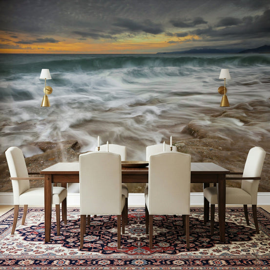 Twilight Tides wallpaper mural of stormy sunset waves behind a wooden dining table and cream chairs on a Persian rug