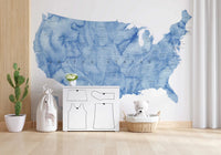 USA map with states and capitals in blue watercolor wallpaper mural in a nursery with a dresser and teddy bear basket