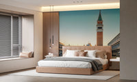 Venetian Sunrise wallpaper mural of St Mark's tower at dawn behind a camel upholstered bed in a bedroom