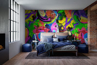 Vibrant Graffiti Splash wallpaper mural in neon tones behind a bed with blue bedding and exposed brick in an industrial bedroom