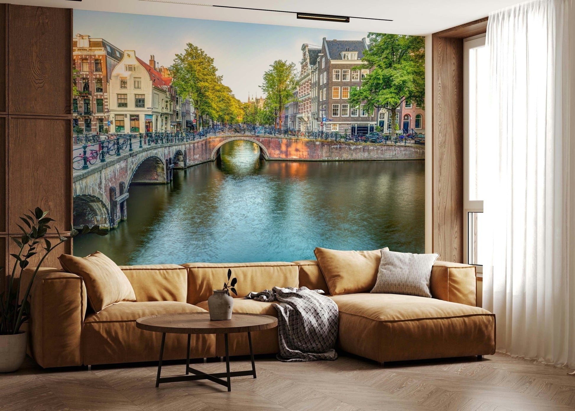 Visit Amsterdam wallpaper mural of a canal and stone bridge behind a tan sectional sofa in a living room