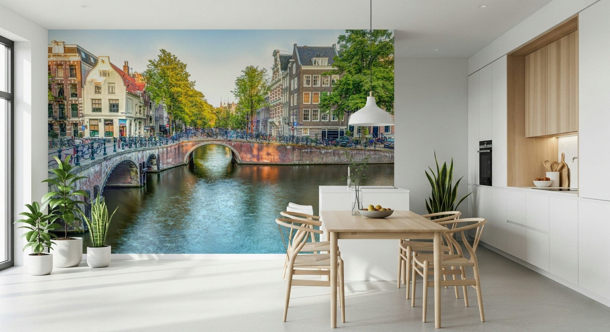 Visit Amsterdam wallpaper mural of canal houses behind a wood dining table with wishbone chairs and plants