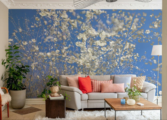 White Blossoms Against a Clear Blue Sky spring nature photography wall mural behind a gray sofa with coral pillows in a bright living room
