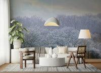Winter's Whispers wallpaper mural of frost-covered trees behind a cream sofa and monstera plant in a living room