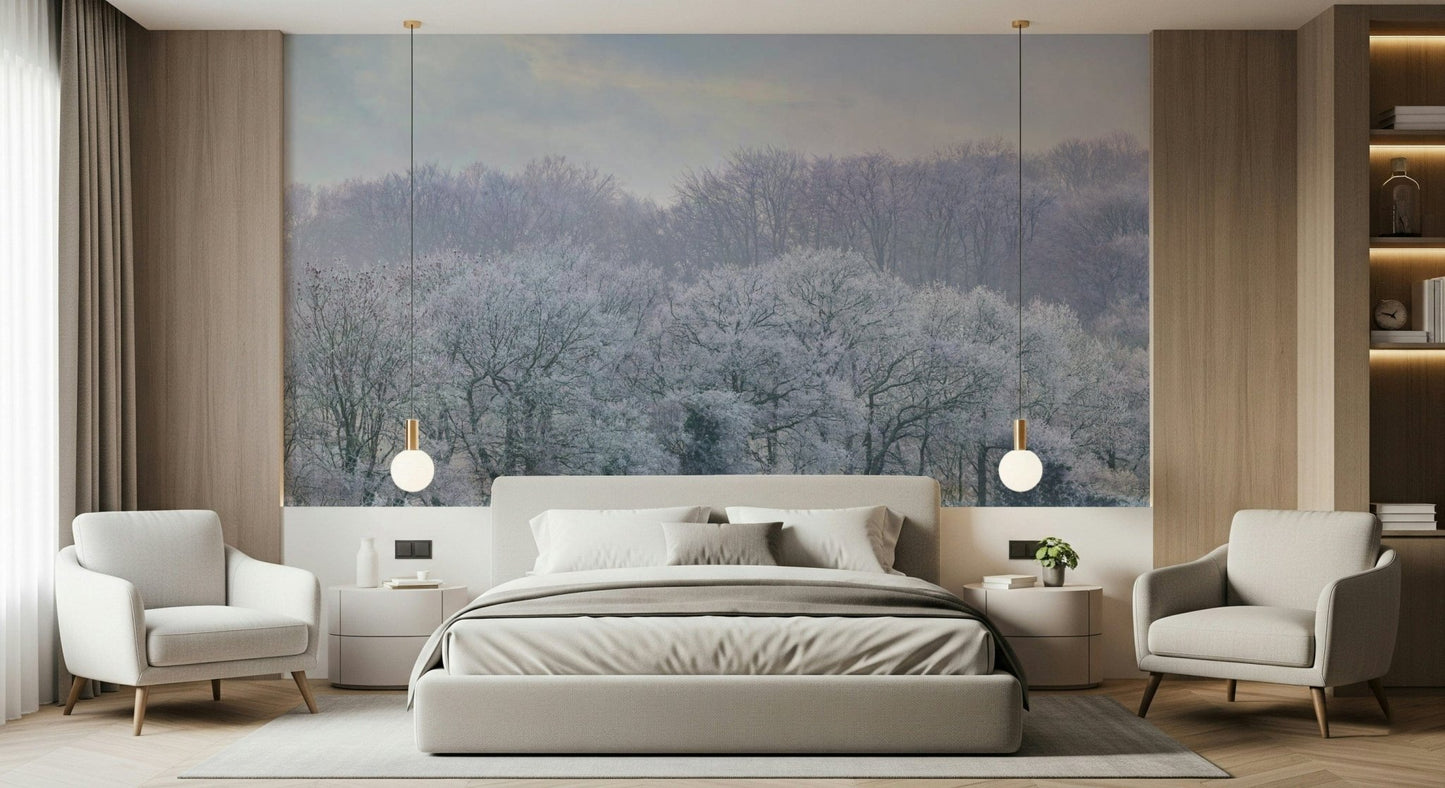 Winter's Whispers wallpaper mural of a frosted woodland under a pale sky behind a grey bed and two cream armchairs