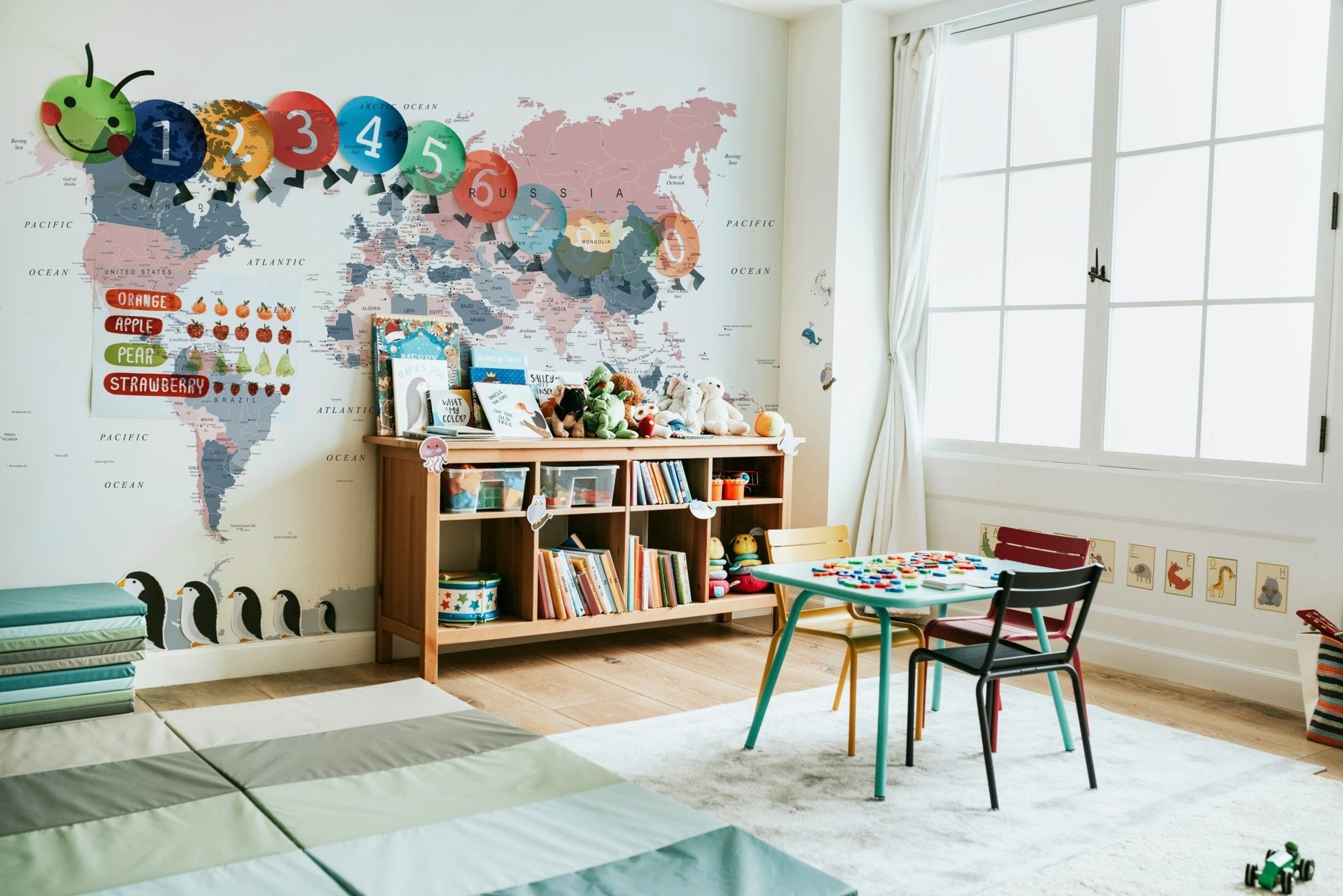 World Map Blush Pink and Indigo wallpaper mural in a kids classroom with a bookshelf and small green table